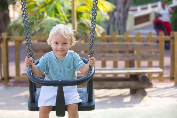 Little toddler boy, playing at the playground summertime, swingi — 스톡 사진