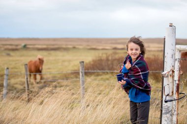 Güzel çocuk, çok rüzgarlı bir günde yolda duruyor, sarılmış.