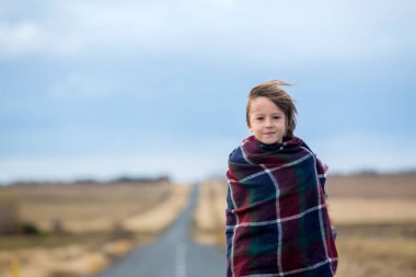 Güzel çocuk, çok rüzgarlı bir günde yolda duruyor, sarılmış.