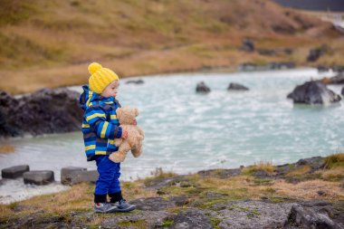 Oyuncak ayıyla küçük bir çocuk, sıcak bir w 'nin önünde duruyor.