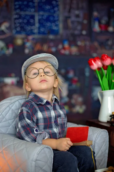 Dulce niño, con gafas, leyendo un libro y bebiendo —  Fotos de Stock