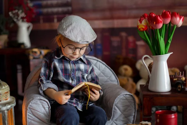 Söta småbarn pojke, bära glasögon, läsa en bok och dricka — Stockfoto