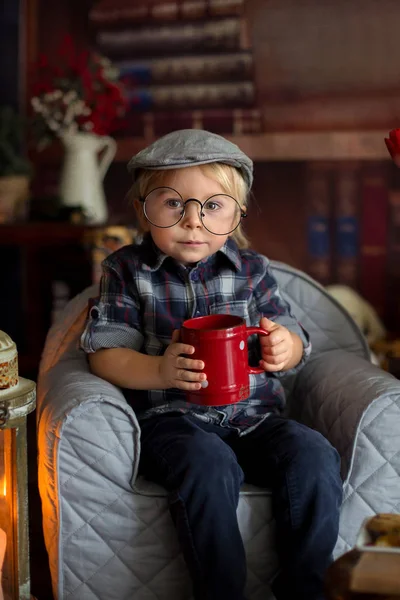 Tatlı çocuk, gözlük takıyor, kitap okuyor ve içiyor. — Stok fotoğraf
