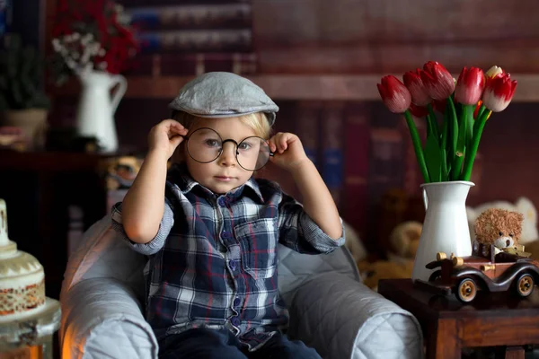 Süßer kleiner Junge, trägt eine Brille, liest ein Buch und trinkt — Stockfoto