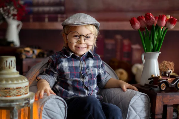 Menino doce, usando óculos, lendo um livro e bebendo — Fotografia de Stock
