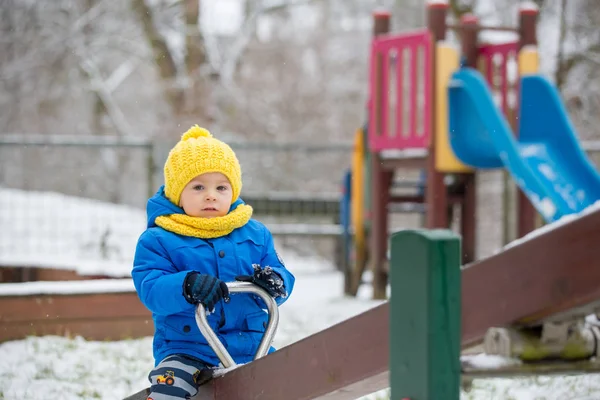 Süßer kleiner Junge, der auf Spielplatz mit Schnee spielt — Stockfoto