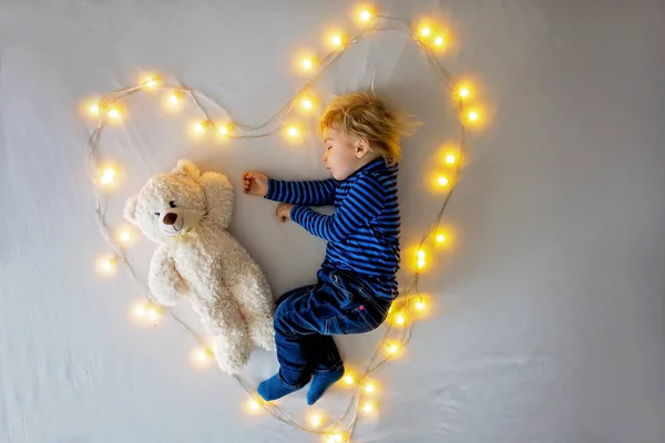 Pequeño niño, durmiendo con osito de peluche en la cama en el corazón hecho b —  Fotos de Stock