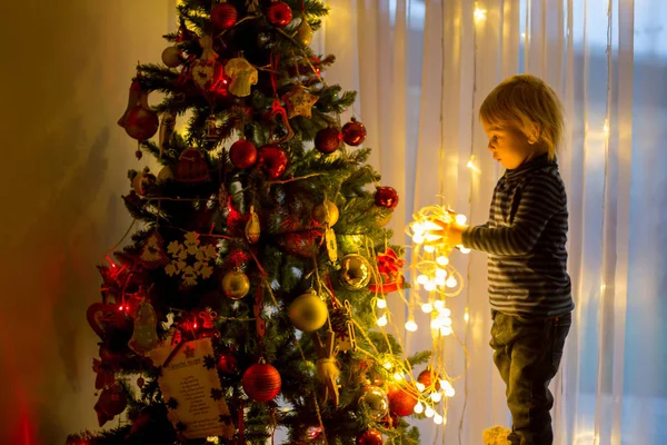 Beautiful blonde toddler boy, decorating christmas tree with bal — Stock Photo, Image