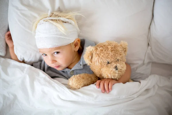 Mały chłopiec z urazem głowy, leżący w łóżku, zmęczony — Zdjęcie stockowe