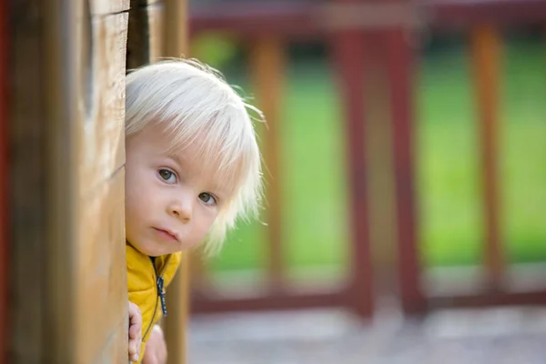 Blonďaté malé batole dítě ve žluté bundě, hraje na plotě — Stock fotografie