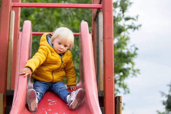 Blondes kleines Kleinkind in gelber Jacke spielt auf dem Pla — Stockfoto