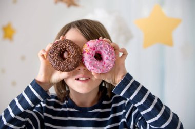 Tatlı sarışın çocuk, oynuyor ve donut yiyor. 
