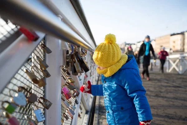 Aranyos kisgyerek, szerelmes zárakat néz, egy hídra zárva. — Stock Fotó