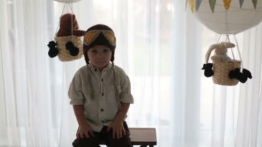 Sweet toddler boy, playing with airplane and teddy bear, decorated air balloons with toys behind him