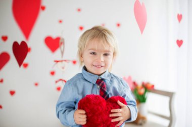 Cute blonde toddler boy, holding heart toy and playing with hear