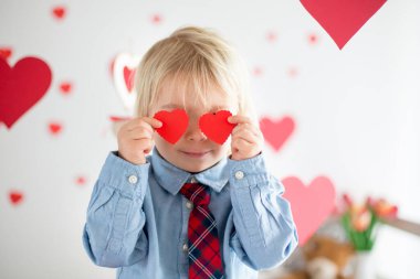 Cute blonde toddler boy, holding heart toy and playing with hear