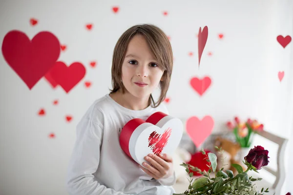 Χαριτωμένο μακρυμάλλη αγόρι σχολείο, κρατώντας κουτί καρδιά και κόκκινα τριαντάφυλλα και — Φωτογραφία Αρχείου
