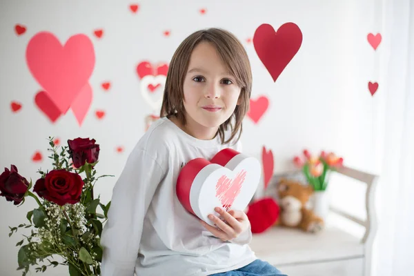 Bonito menino da escola de cabelos longos, segurando caixa de coração e rosas vermelhas e — Fotografia de Stock