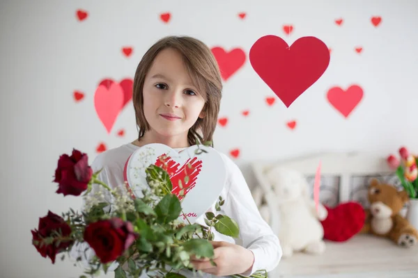 Lindo niño de pelo largo de la escuela, la celebración de la caja del corazón y rosas rojas y —  Fotos de Stock