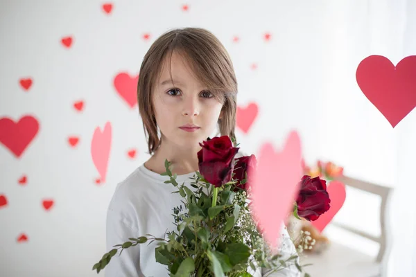 Lindo niño de pelo largo de la escuela, la celebración de la caja del corazón y rosas rojas y —  Fotos de Stock