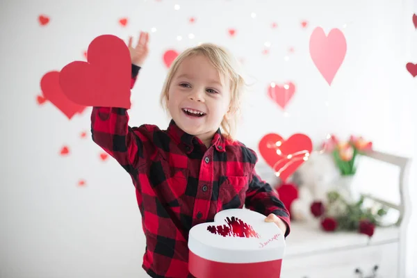 Cute blonde toddler boy, holding box in heart shape and flowers — Stok fotoğraf