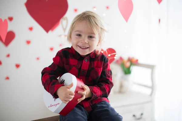 Leuke blonde peuter jongen, holding box in hart vorm en bloemen — Stockfoto