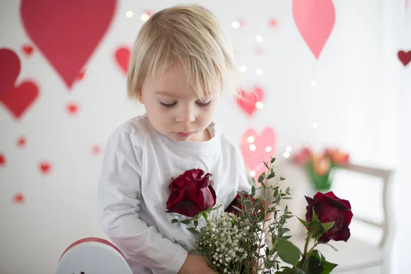 Cute blonde toddler boy, holding box in heart shape and flowers — Stok fotoğraf