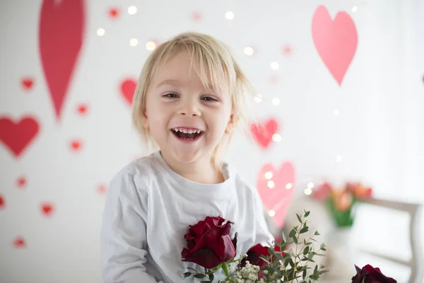 Leuke blonde peuter jongen, holding box in hart vorm en bloemen — Stockfoto