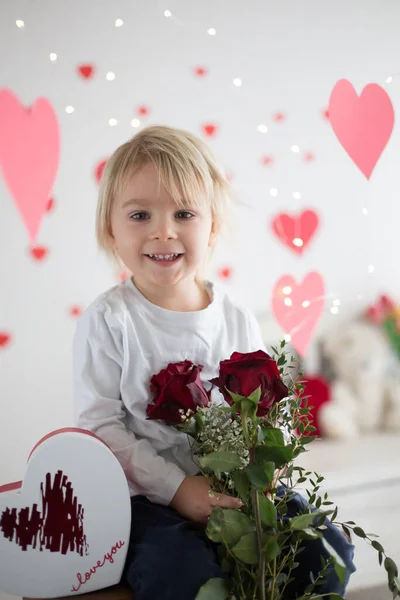 Cute blonde toddler boy, holding box in heart shape and flowers — ストック写真