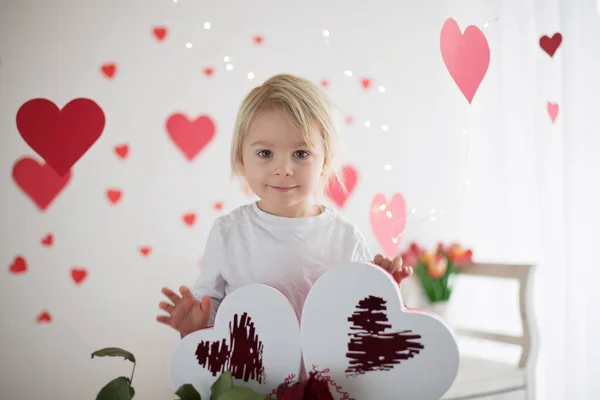 Cute blonde toddler boy, holding box in heart shape and flowers — Stok fotoğraf