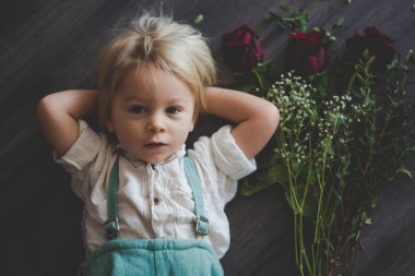 Beautiful toddler boy, holding red roses for mother's day