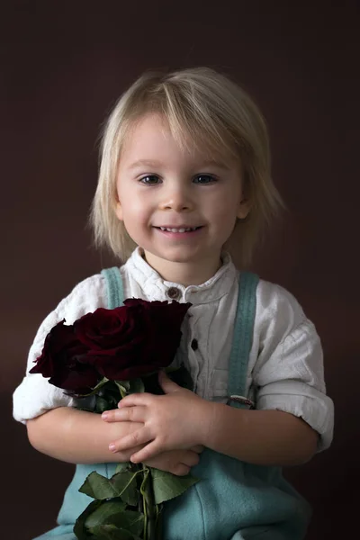 Beautiful toddler boy, holding red roses for mother's day — Stockfoto