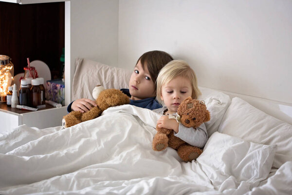 Sick children, toddler and older boy, brothers, lying in bed with a fever, resting