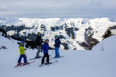 Aile, güneşli bir günde kayak merkezinde kayak yapmak, manzaranın tadını çıkarmak.