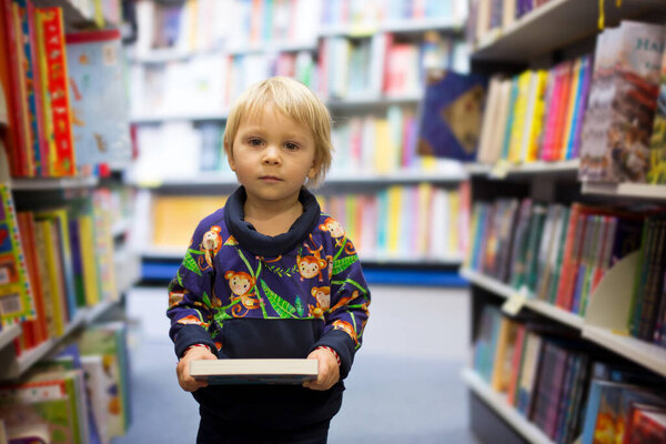 Adorable little boy, sitting in a book store and read book