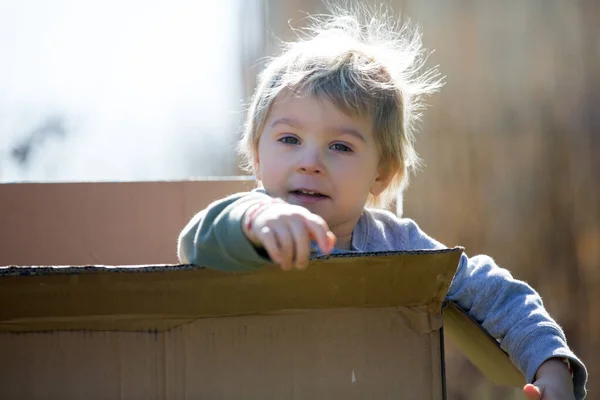 可爱的幼儿 可爱的金发男孩 躲在纸板箱里 从洞里往外看 面带微笑 — 图库照片