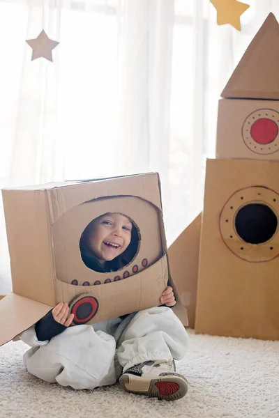 宇宙飛行士の格好をした甘い幼児の男の子は 段ボールロケットと手作りのヘルメットを箱から家で遊んでいます — ストック写真