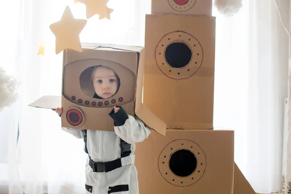 宇宙飛行士の格好をした甘い幼児の男の子は 段ボールロケットと手作りのヘルメットを箱から家で遊んでいます — ストック写真