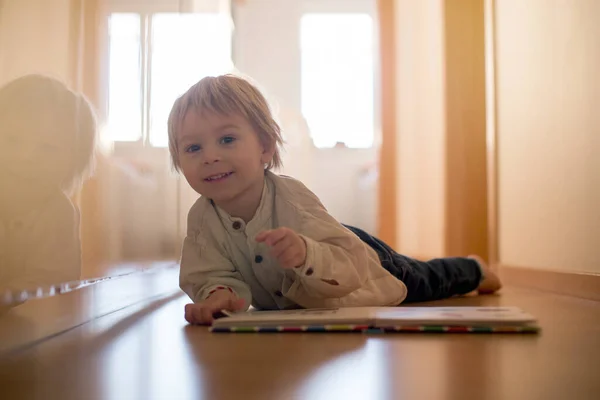 美しい幼児ブロンドの少年は ホールの自宅の床に横たわって 本を読んで 美しいバックライト — ストック写真