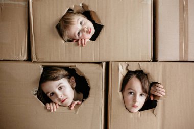 Tatlı çocuklar, erkek kardeşler, karton kutuda saklanıyorlar, dışarıyı izliyorlar, izole edilmişler. Üzgün çocuklar, karantinadan dolayı evde kalıp birlikte oynuyorlar.