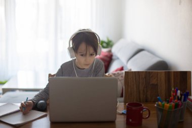 Okul çocuğu, dizüstü bilgisayarla masada oturuyor, evde eğitim görürken okul Coronavirus yüzünden kapalıyken okul ödevlerini yazıyor.