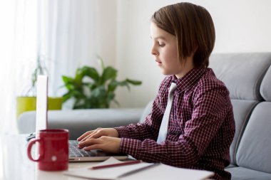 Okul çocuğu, dizüstü bilgisayarla masada oturuyor, evde eğitim görürken okul Coronavirus yüzünden kapalıyken okul ödevlerini yazıyor.