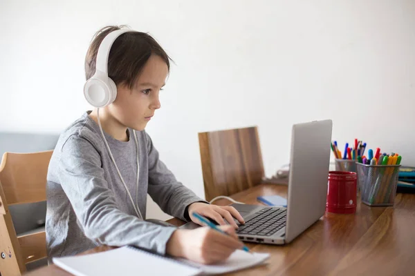 学校はコロナウイルスのため閉鎖されている間 学校の子供は ノートパソコンでテーブルに座って 学校のタスクを書き込みます — ストック写真
