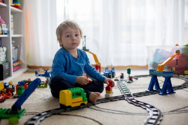 Evde renkli plastik inşaat bloklarıyla oynayan sevimli küçük çocuk yerde oturuyor, tren raylara çıkıyor. Çocuklar için yaratıcı oyunlar