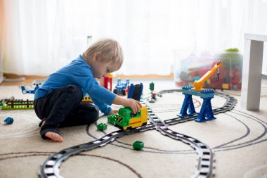 Evde renkli plastik inşaat bloklarıyla oynayan sevimli küçük çocuk yerde oturuyor, tren raylara çıkıyor. Çocuklar için yaratıcı oyunlar