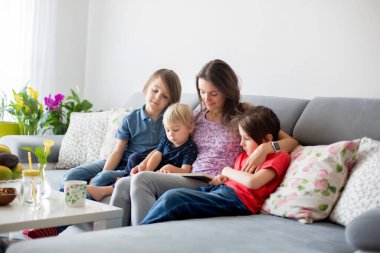 Genç bir kadın, üç çocuklu bir anne, evde kitap okuyor, sarılıyor ve gülüyor, aile mutluluğu.