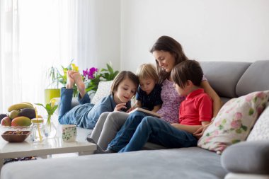 Genç bir kadın, üç çocuklu bir anne, evde kitap okuyor, sarılıyor ve gülüyor, aile mutluluğu.