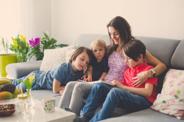 Genç bir kadın, üç çocuklu bir anne, evde kitap okuyor, sarılıyor ve gülüyor, aile mutluluğu.