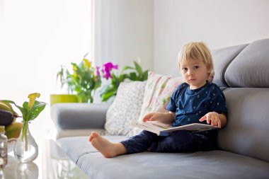 Tatlı sarışın çocuk, evde kitap okuyor, gülüyor, aile mutluluğu.