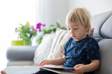 Tatlı sarışın çocuk, evde kitap okuyor, gülüyor, aile mutluluğu.